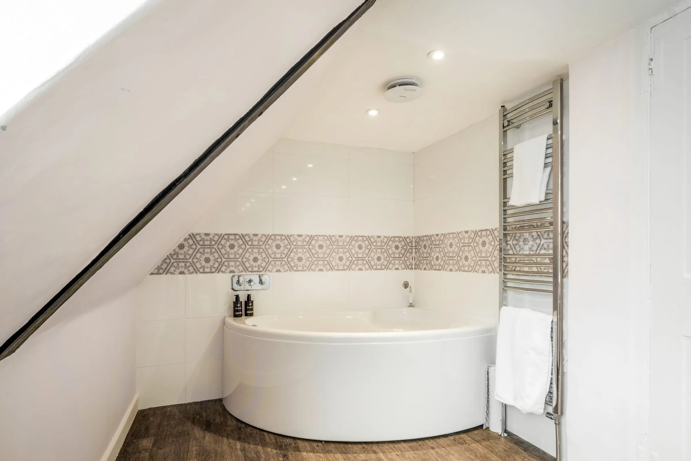 Corner bath under the eaves with patterned tile border and heated towel rail