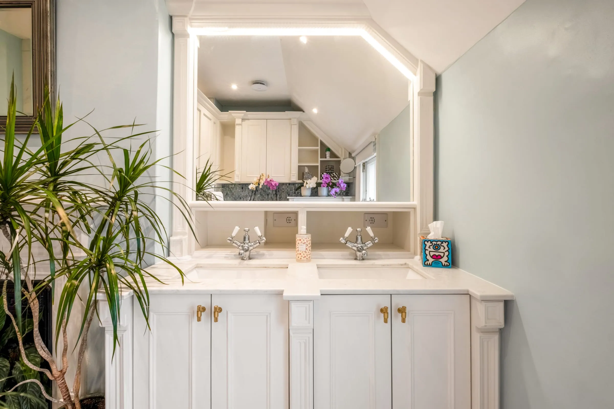 Bathroom with twin basins set in a white vanity unit, large mirror and plants