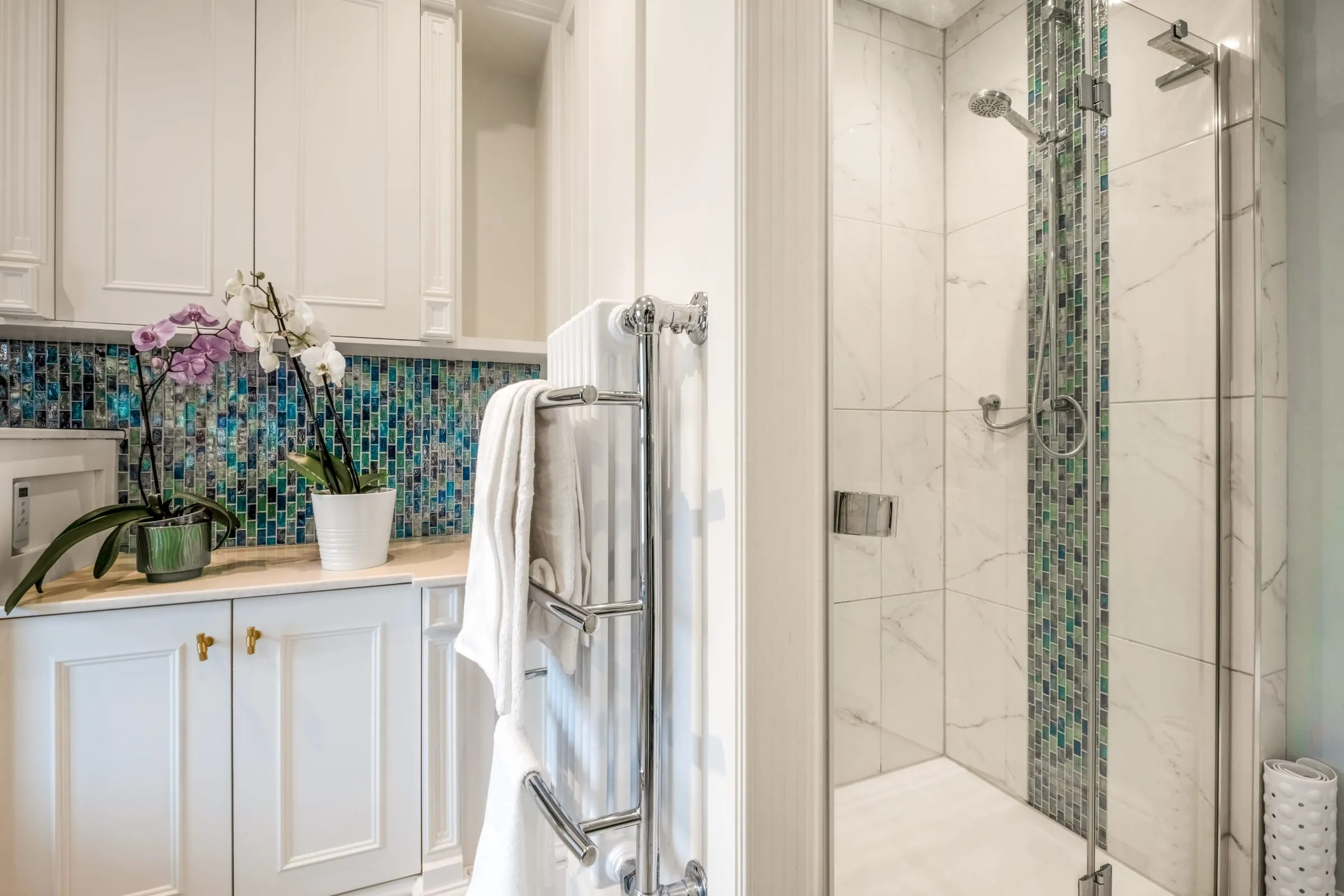 Walk-in shower with mosaic tiling, heated towel rail and orchid on the vanity