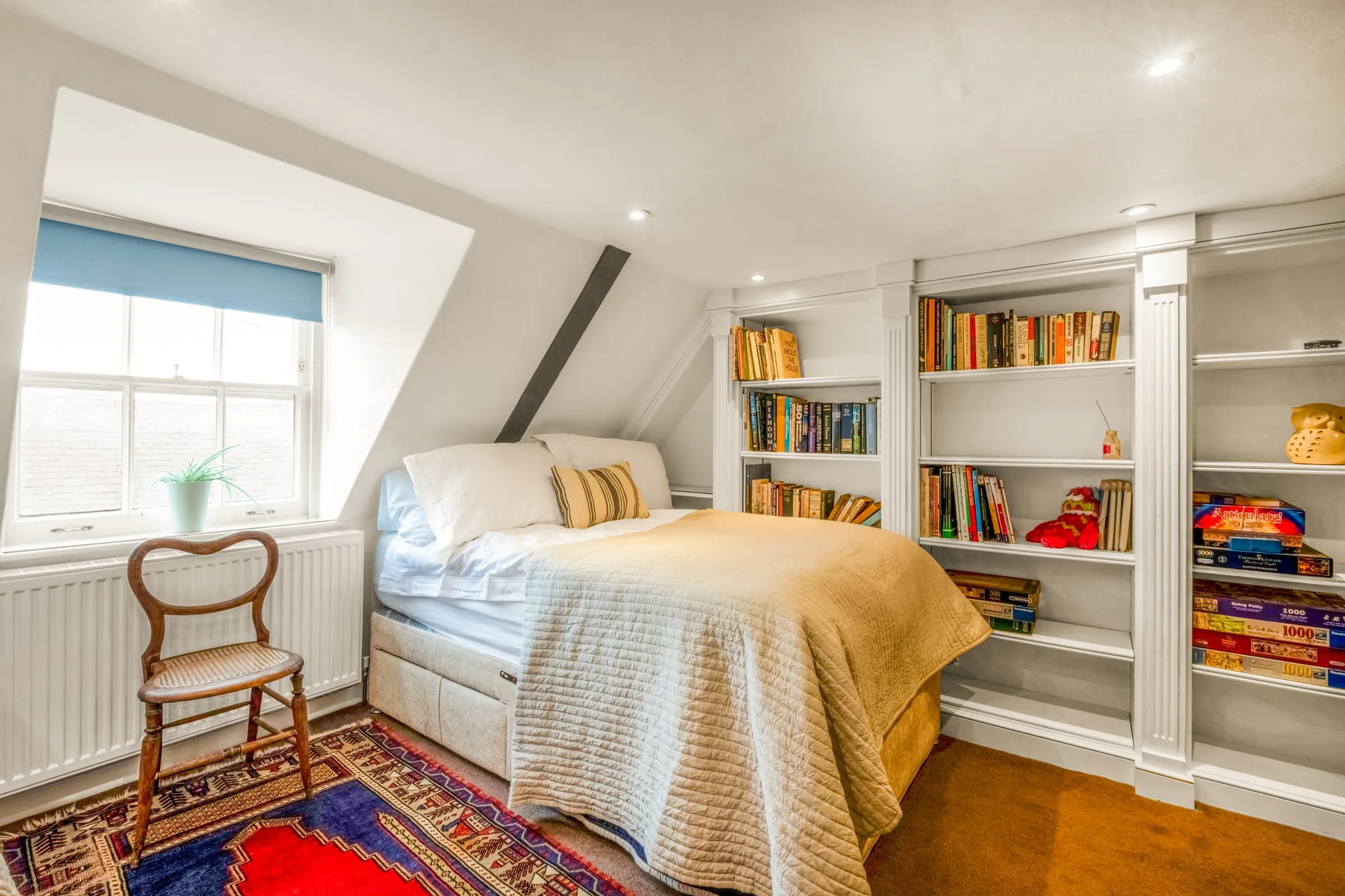 Bedroom with a single bed, built-in bookshelves of books and board games, and a sash window