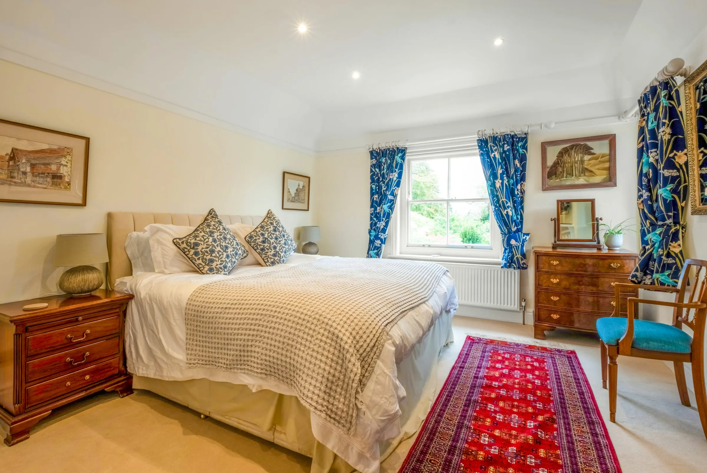 Bedroom with a double bed, blue patterned curtains, a fireplace and antique chest of drawers