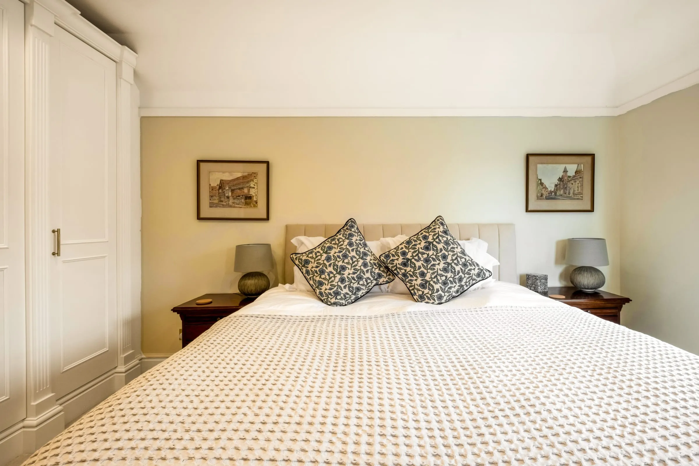 Bedroom with a king-size bed, patterned cushions, bedside lamps and framed prints