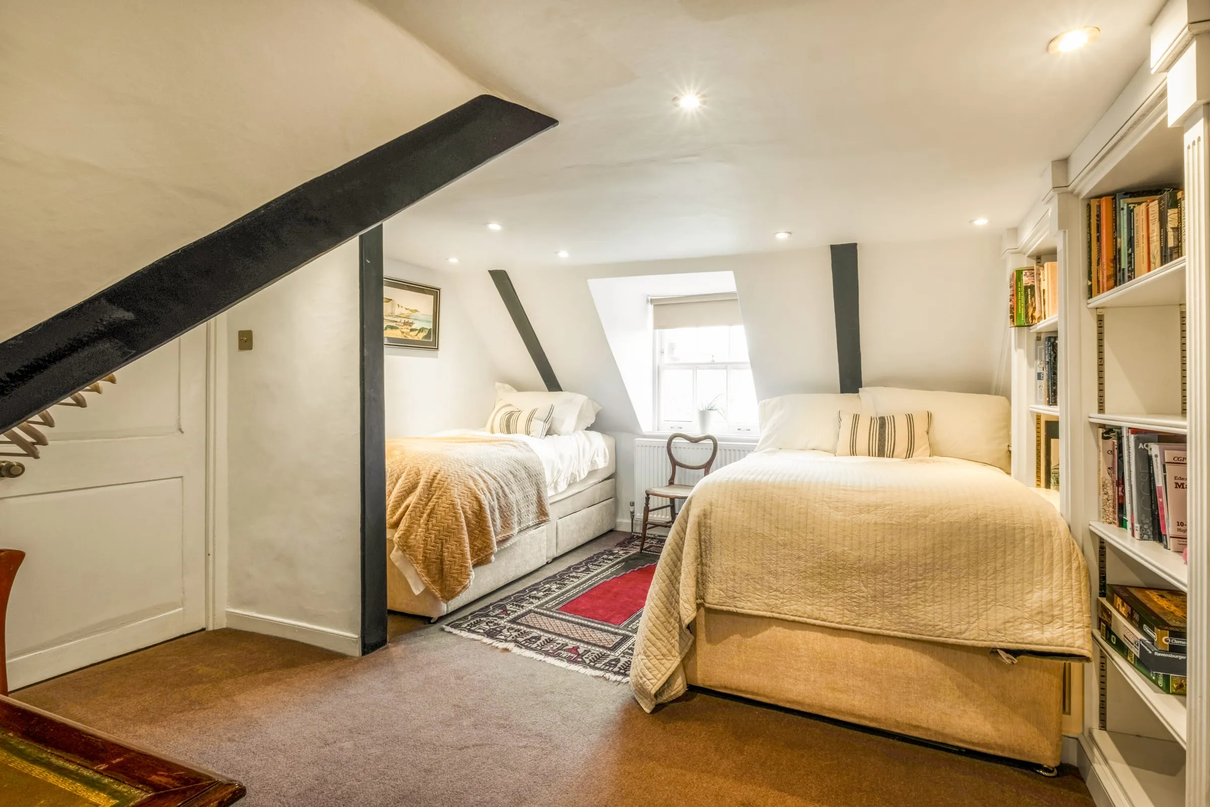 Bedroom with two beds under exposed beams, with bookshelves and a dormer window