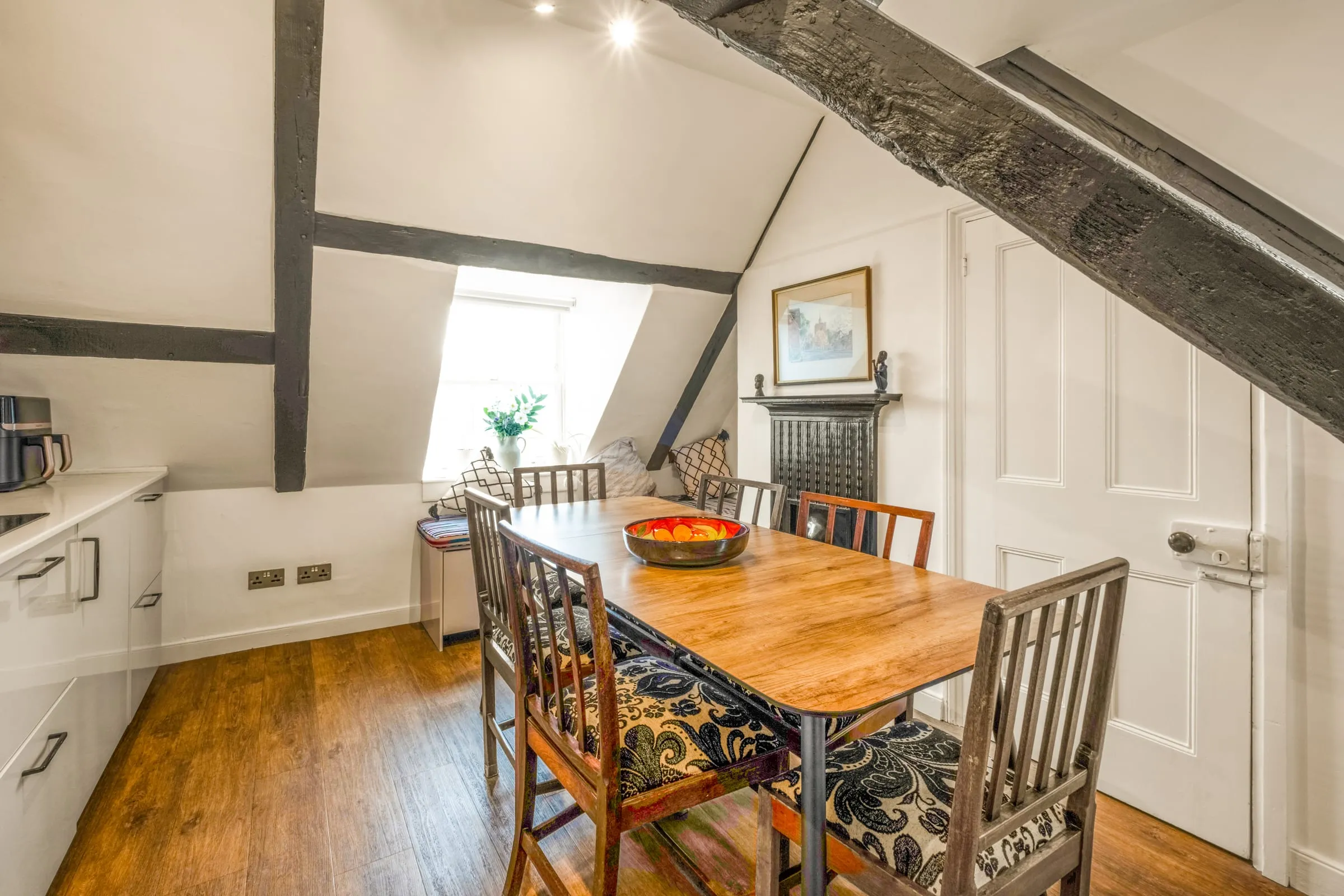 Dining table and chairs under exposed black timber beams beside a window