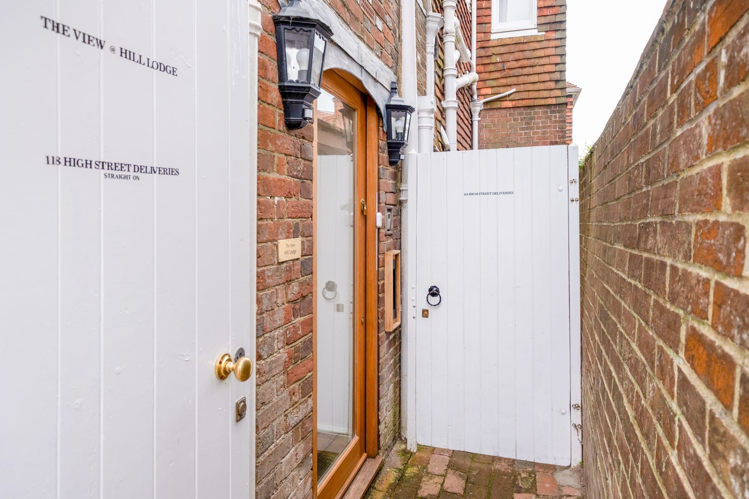 Private entrance: white gate and door beside a brick wall with lantern and delivery sign