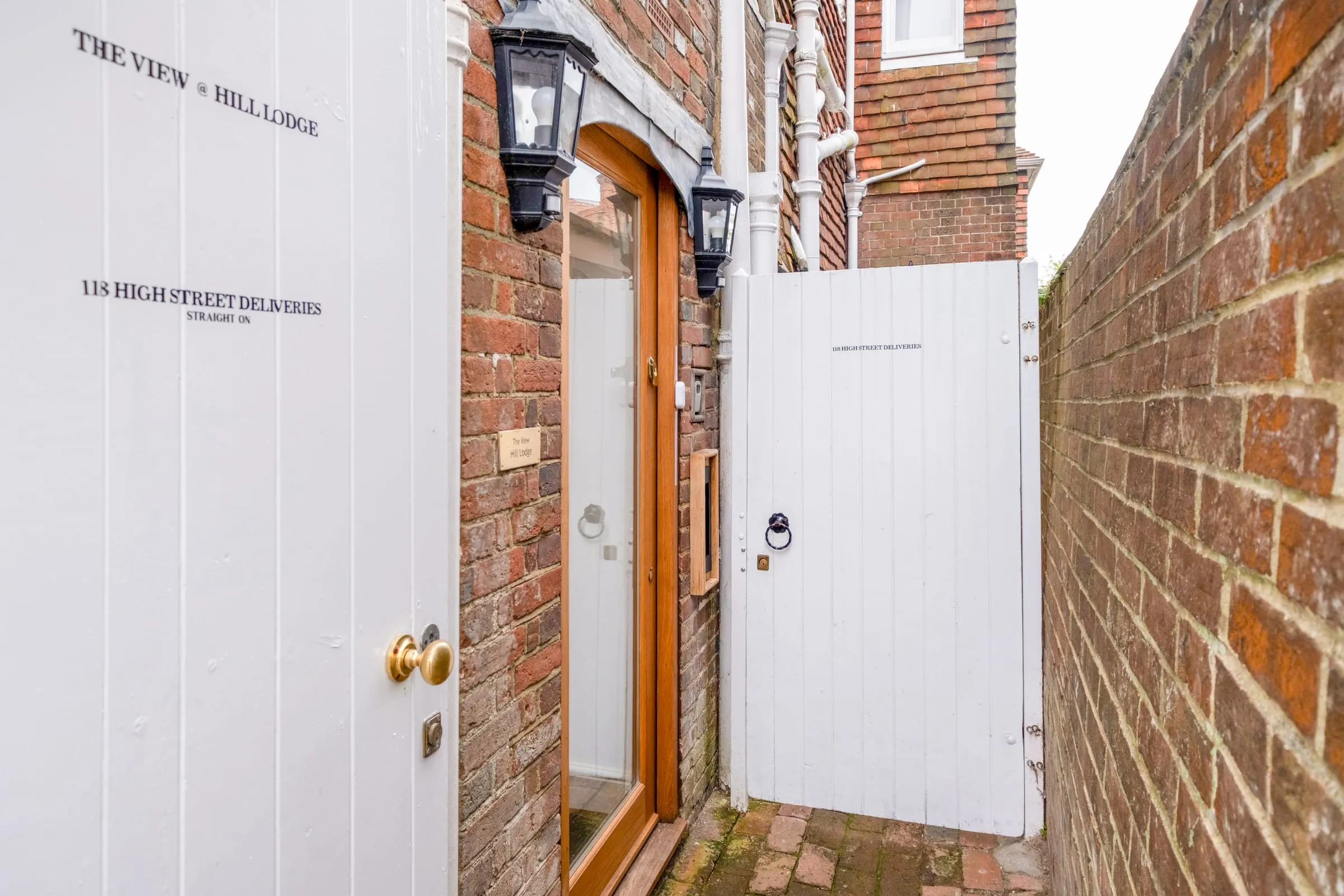 Private entrance: white gate and door beside a brick wall with lantern and delivery sign