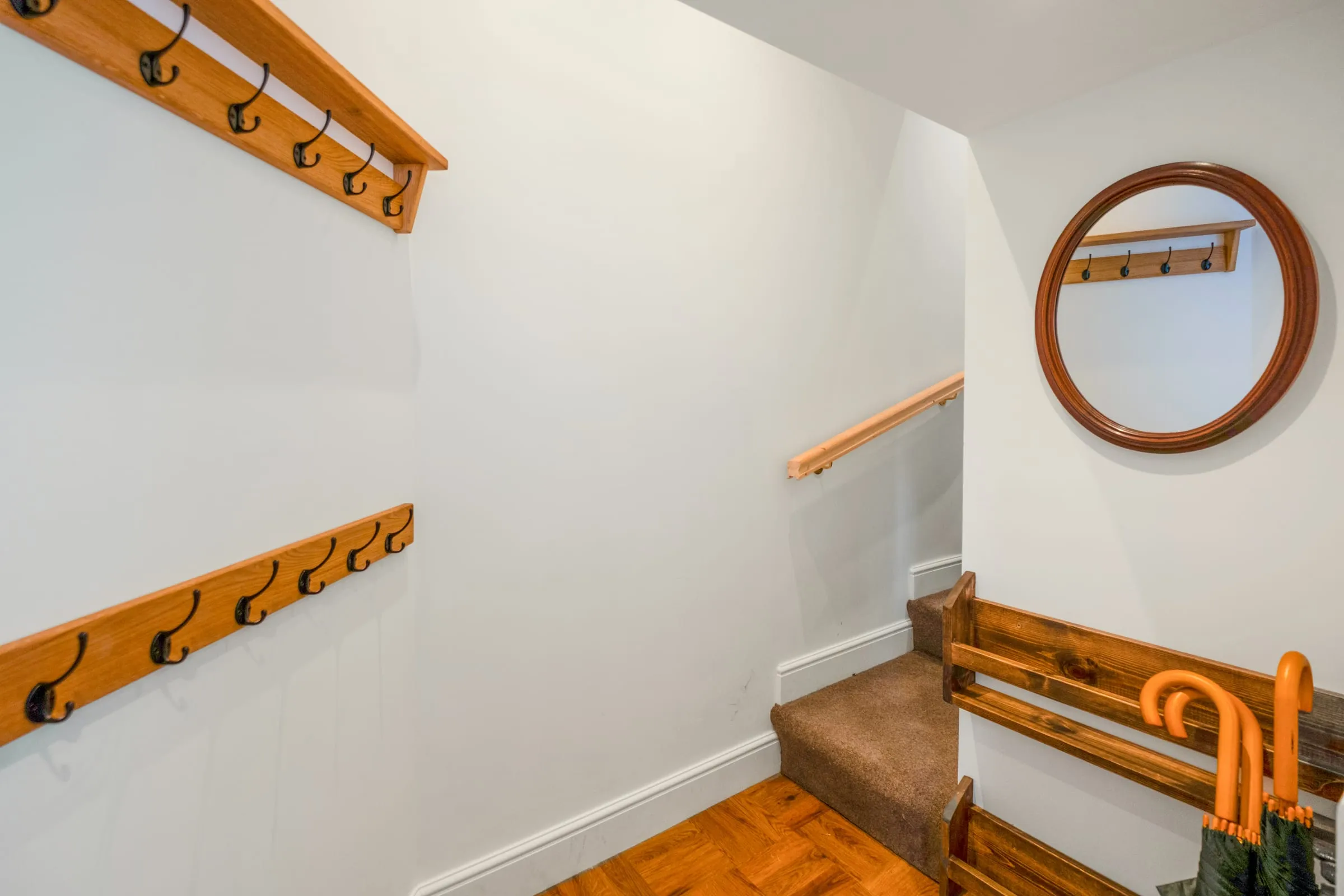 Hallway with coat hooks, round mirror and stairs with wooden handrails