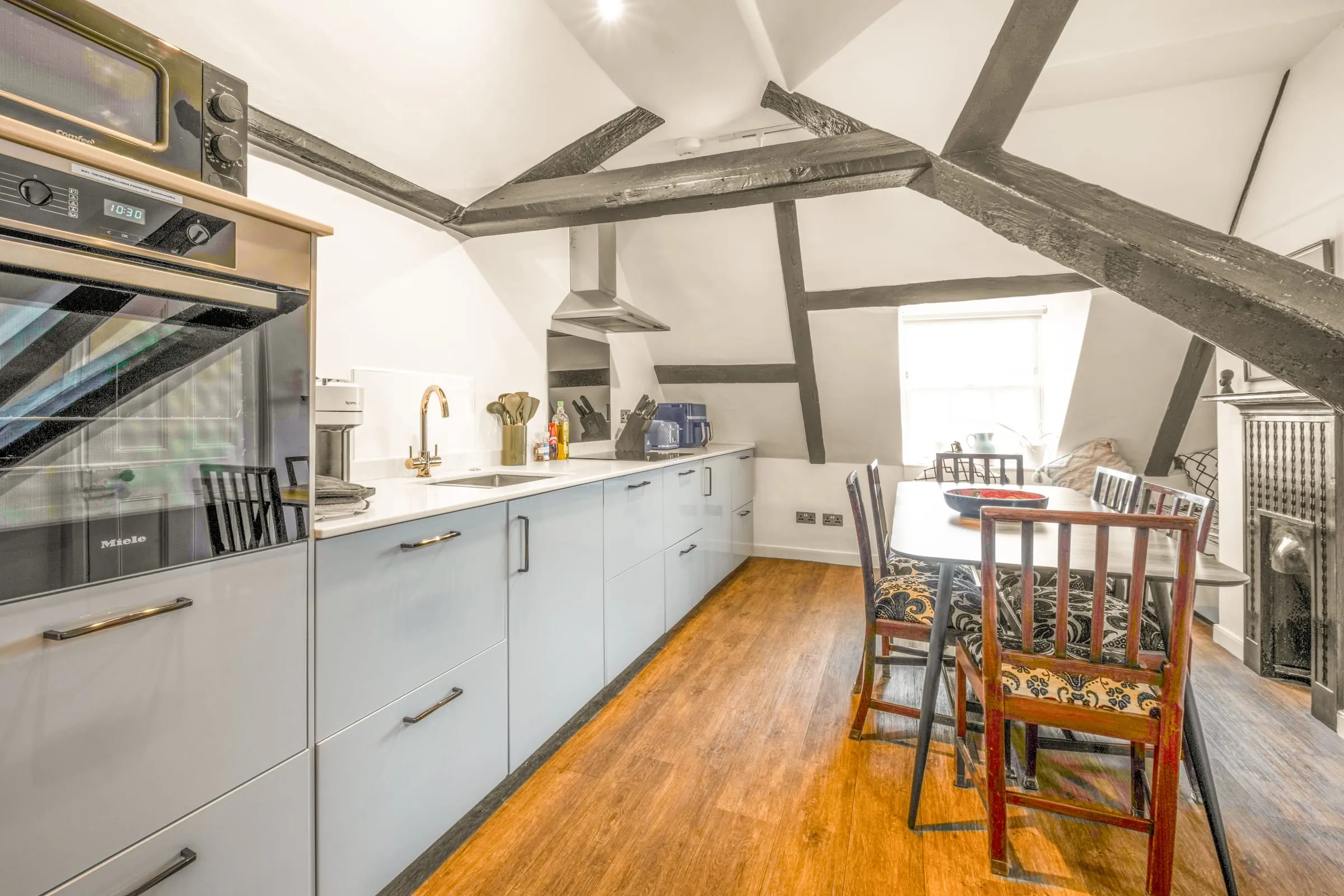 Long kitchen with pale blue units, integrated oven and dining table under the eaves