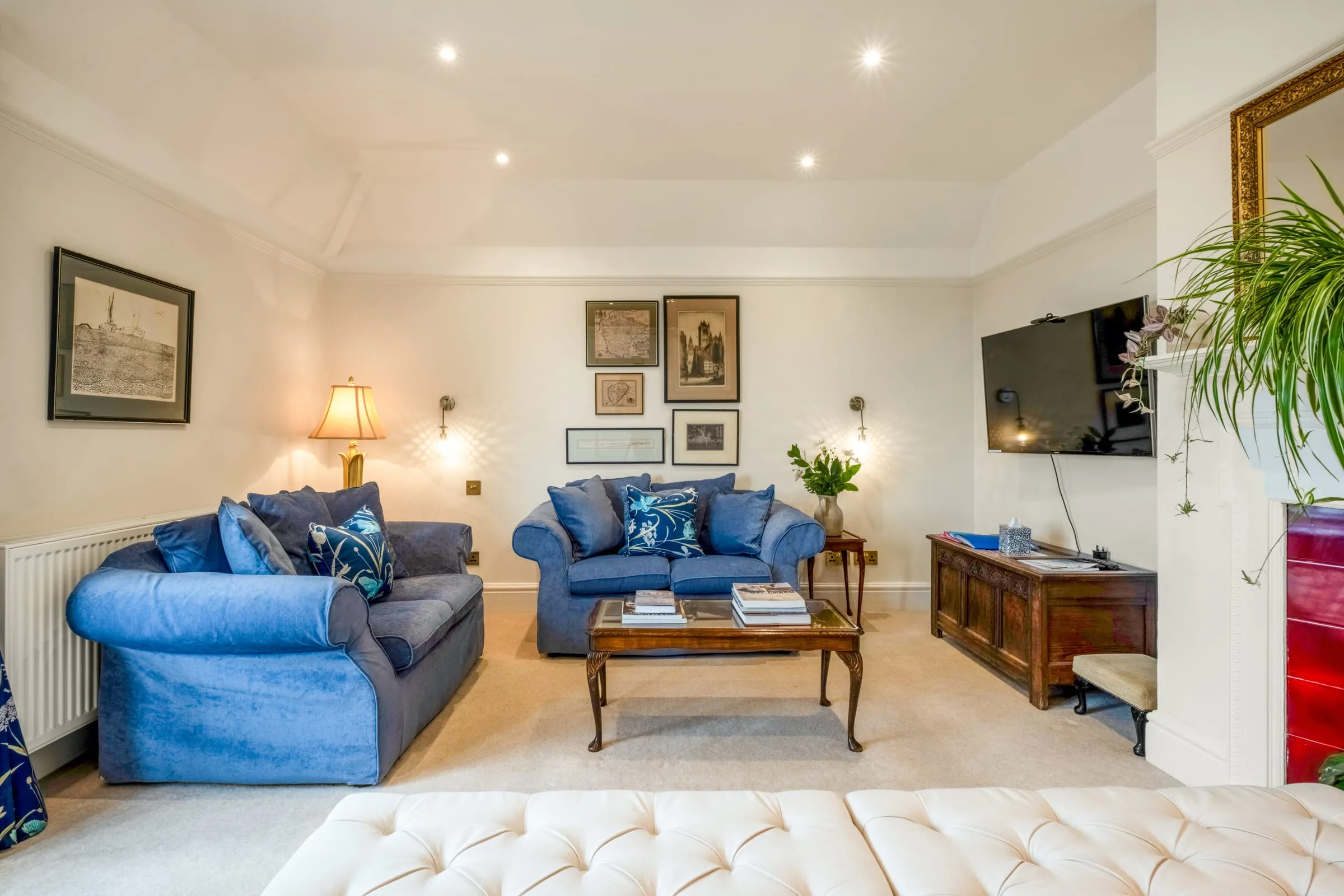 Bright living room with two blue sofas, a wooden coffee table, wall-mounted TV and framed prints