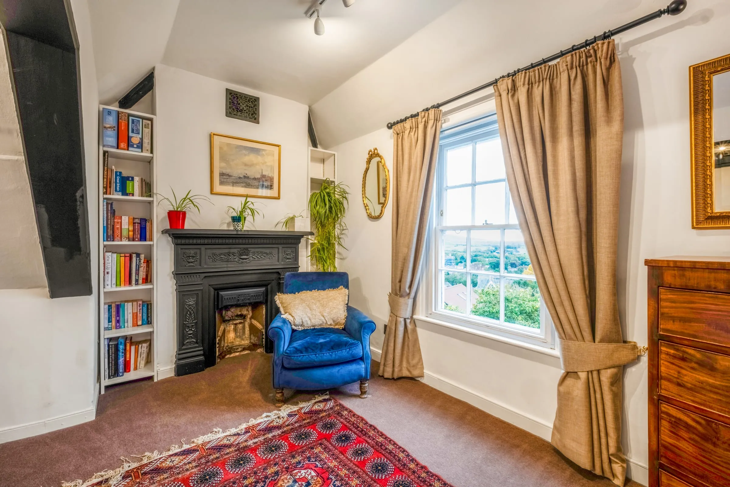 Reading corner with a blue armchair, cast-iron fireplace, full bookshelves and a sash window
