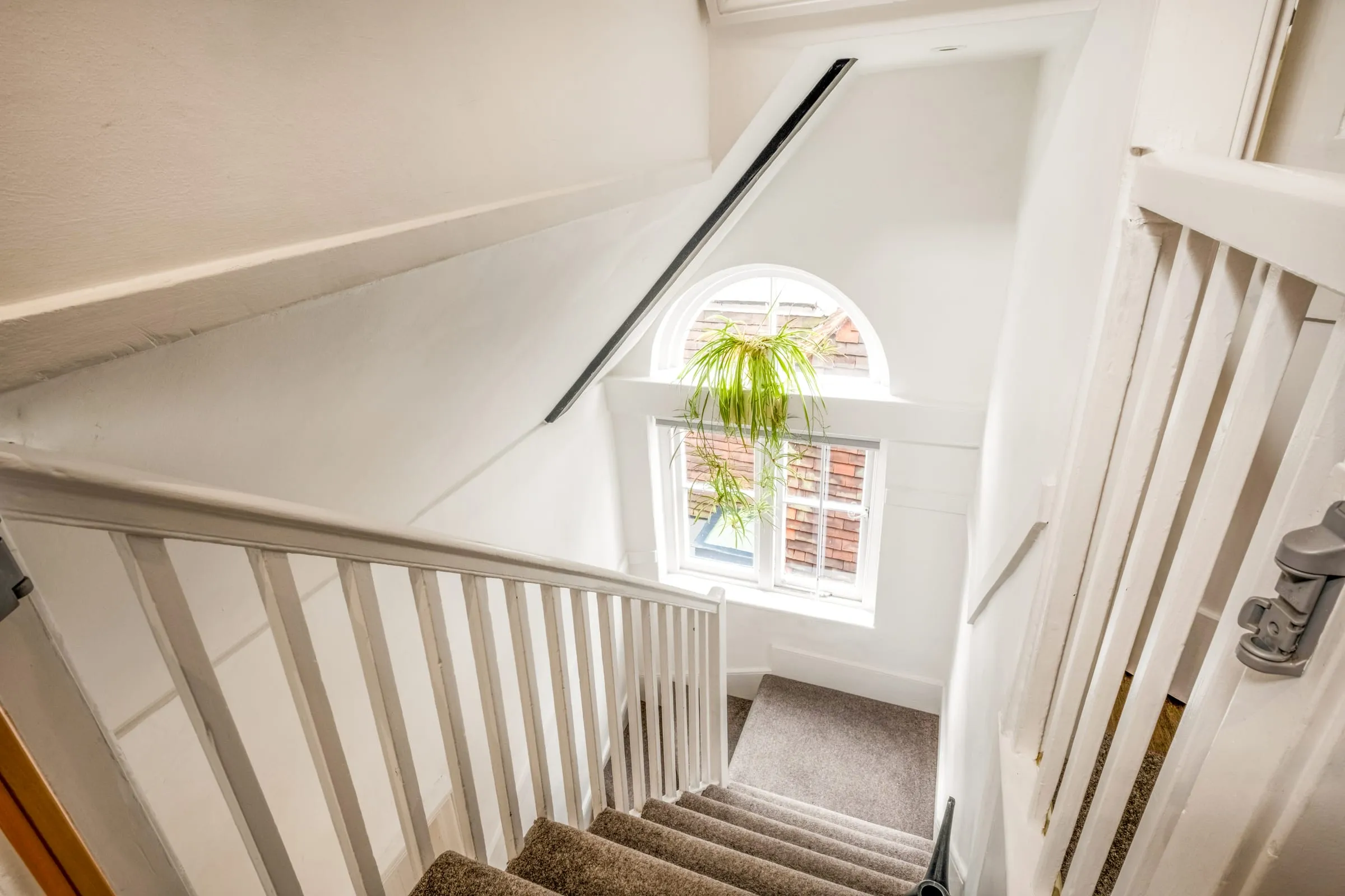 White-painted staircase with an arched window and plant on the sill