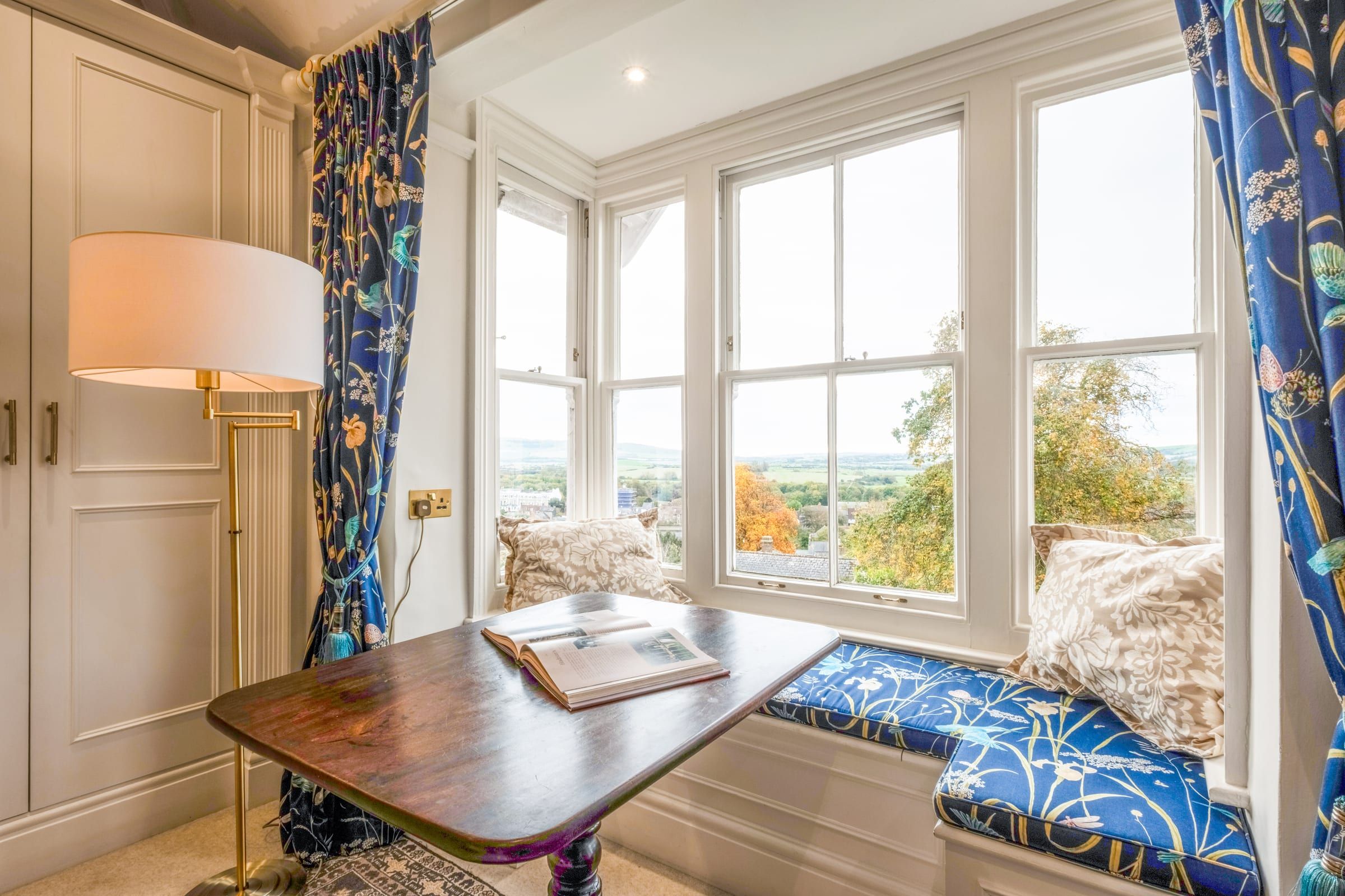 Cushioned window seat beside a Georgian sash window looking out towards the Downs, with a small table and reading lamp
