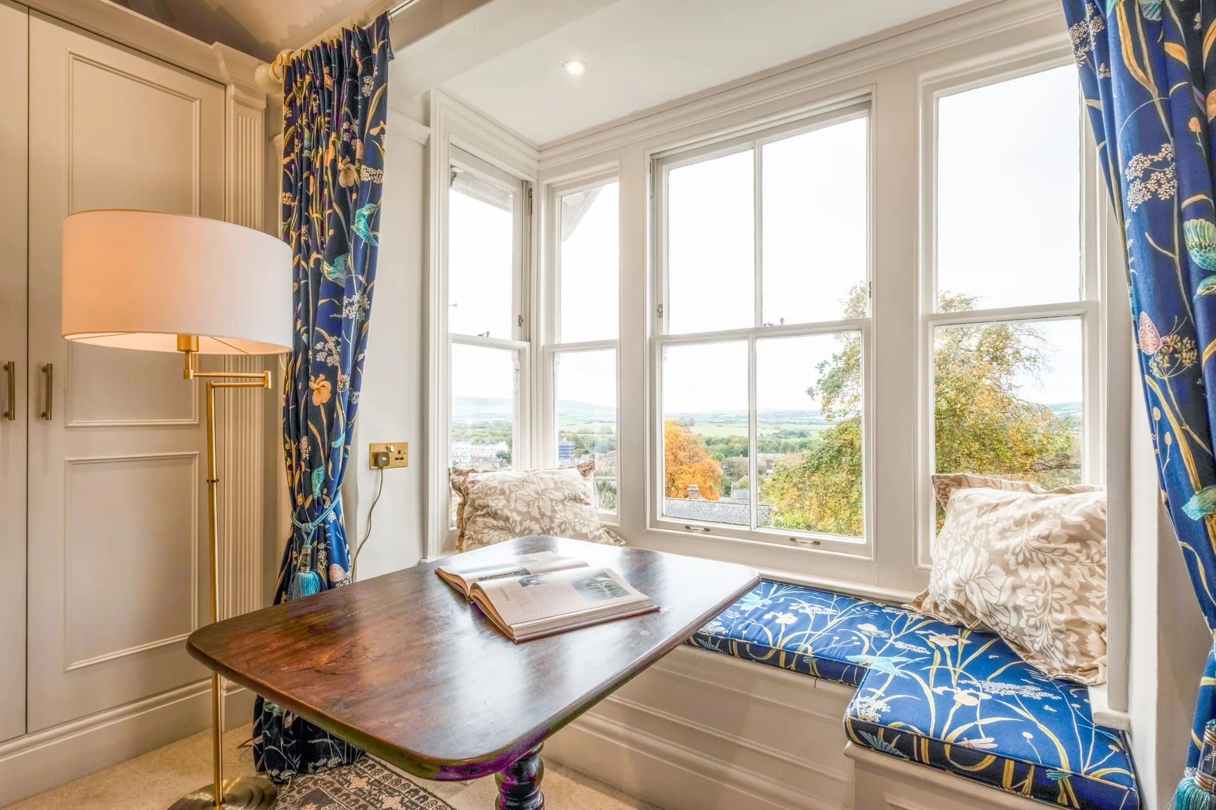 Cushioned window seat beside a Georgian sash window looking out towards the Downs, with a small table and reading lamp